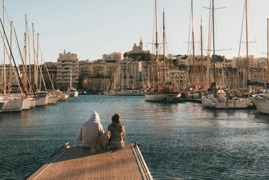 Couple and dog relaxing by the harbor with Marseille skyline.